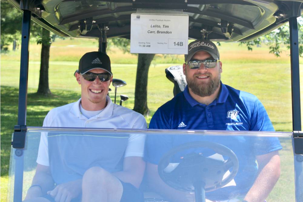 two alumni smile for picture in golf cart